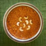 Bright orange carrot halwa in a round serving dish topped with halved cashew nuts. As prepared at The Bangala, Karaikudi.