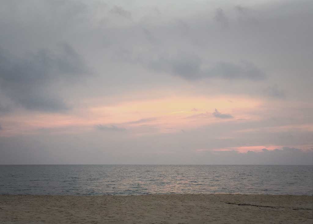 pink clouds over the ocean viewed from a sandy beach